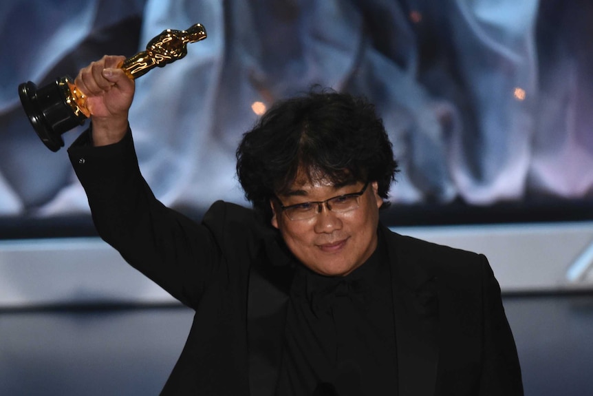 Bong Joon Ho holds his Oscar for best international feature film in the air while on stage at the Academy Awards.