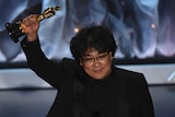Bong Joon Ho holds his Oscar for best international feature film in the air while on stage at the Academy Awards.