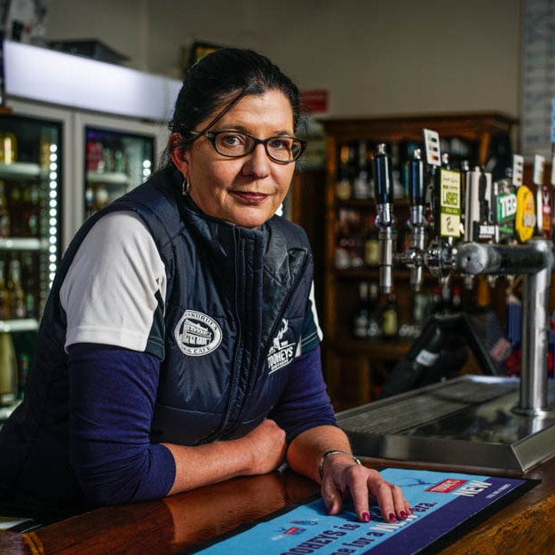 A female publican stands behind the bar at her country hotel