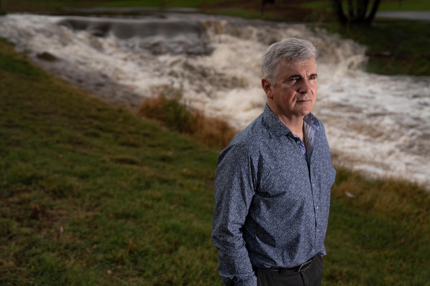 Professor Mark Howden stands almost side-on in front of a rushing river