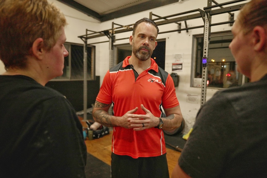 一个男人在健身房里和两个人聊天。 