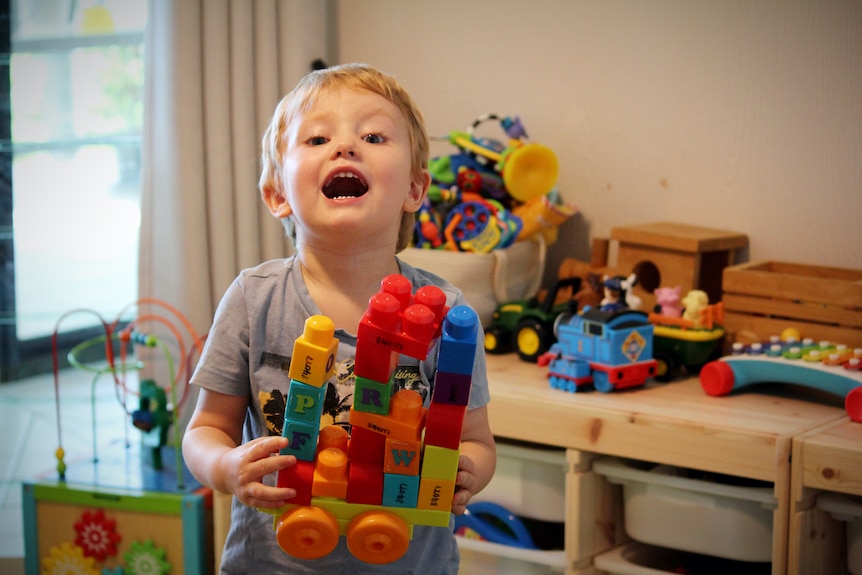 장난감으로 가득 찬 놀이방에 있는 한 유아가 블록으로 만든 다채로운 트럭을 들고 있습니다.