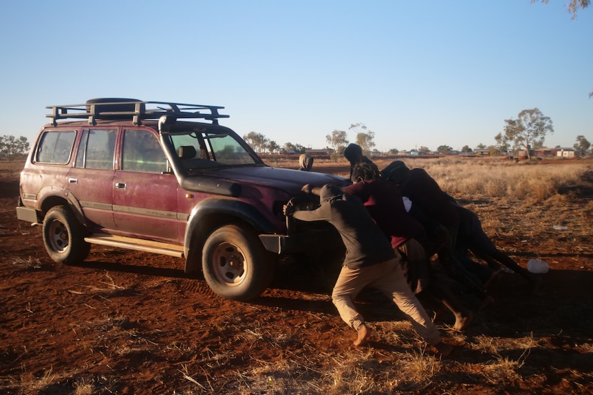 The football team push a red four-wheel drive