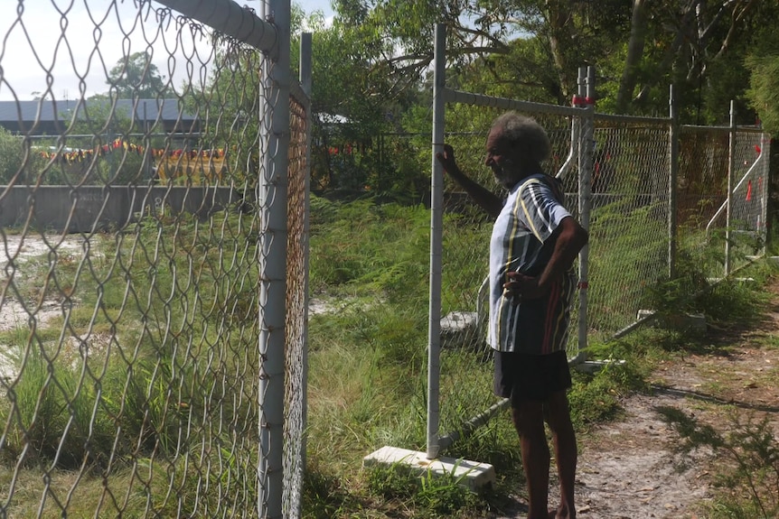 A traditional owner stands at a fence that's sectioned off an area of bushland.