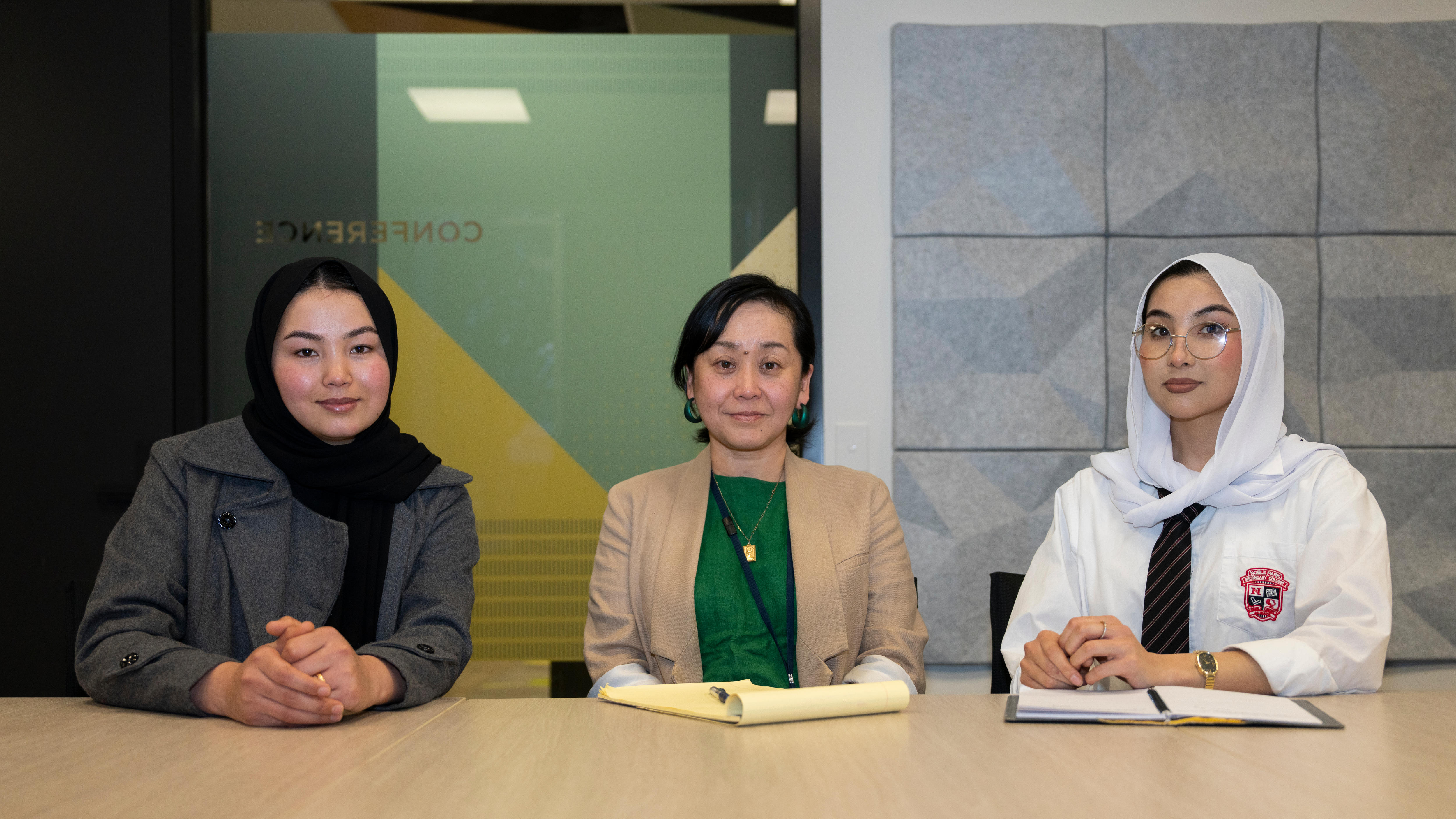 Three women, Adiba, Yoko and Arya, sit behind a table, looking at the camera