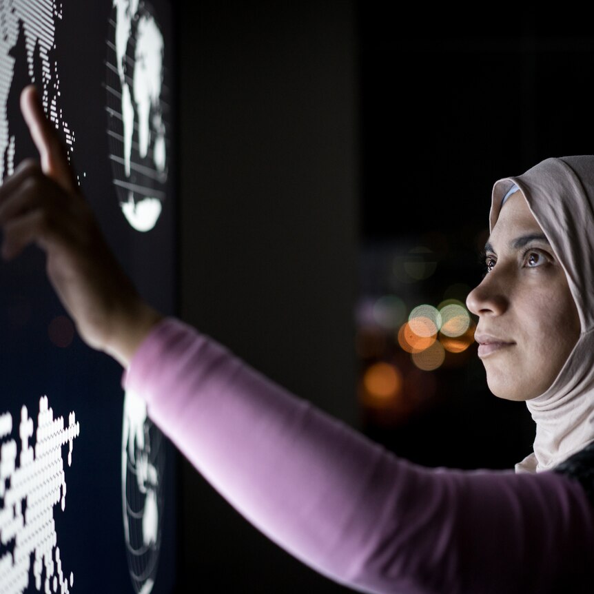 A thoughtful woman wearing a hijab points to a map of the world on a computer screen