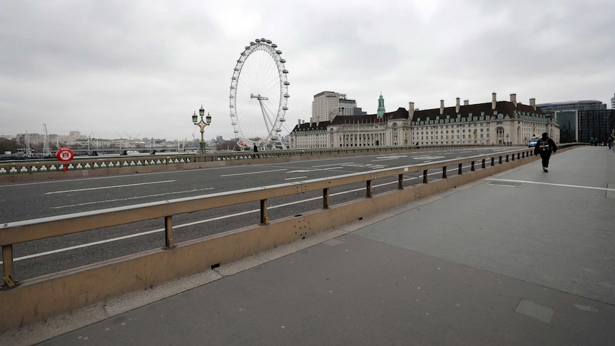 A man walks alone across a bridge overlooking London's big ferris wheel.