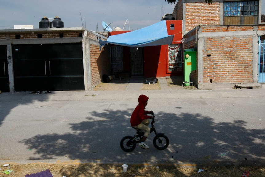 Boy on a bike rides past a front yard of a Mexican house.