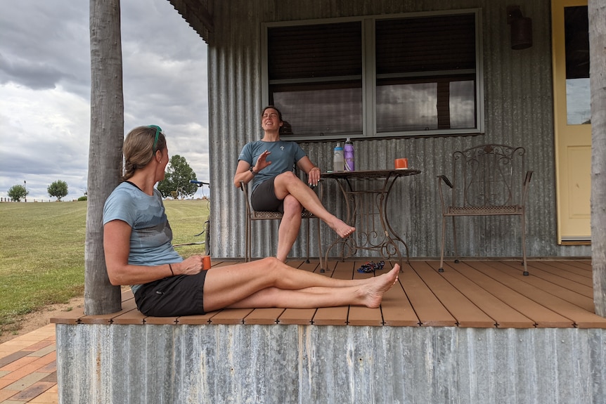 Two women sit on the verandah of a farmhouse.