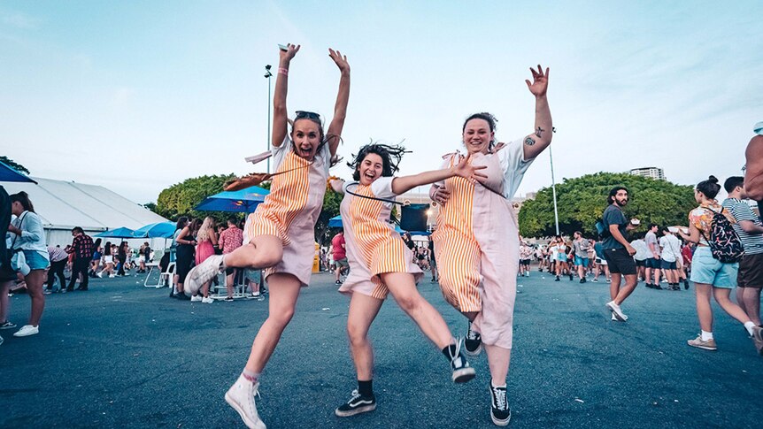 Three laughing women in matching outfits jump in the air