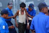 An asylum seeker is escorted off his boat