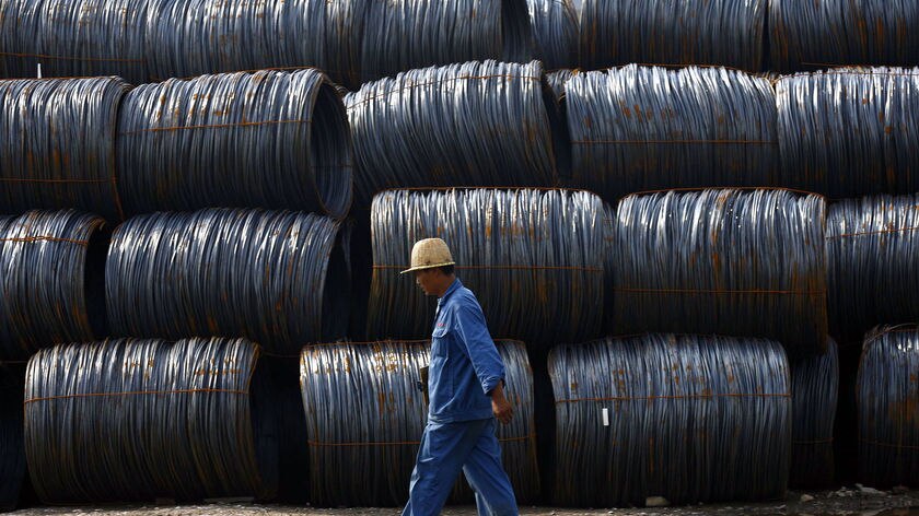 A worker walks by the pile of steel at an iron and steel mill yard in Hefei, central China's Anhui province