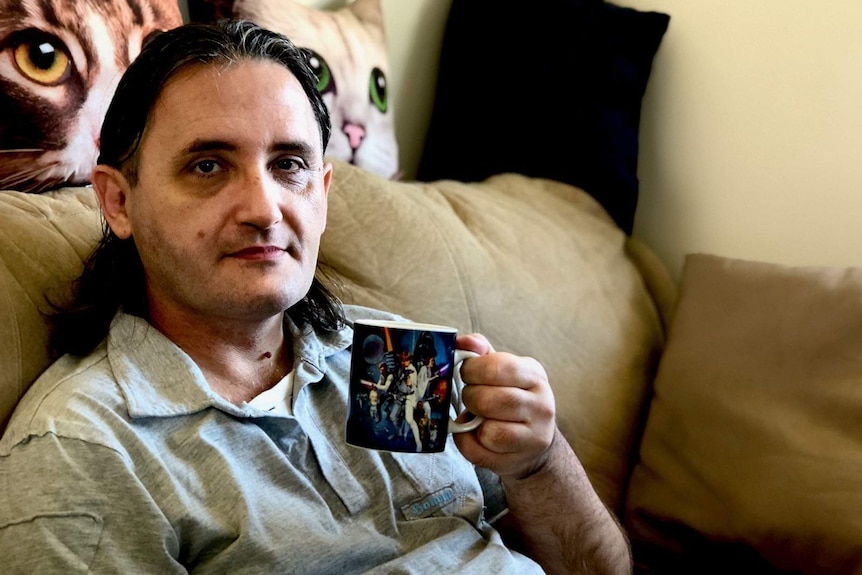 A man sitting on a couch in his home, drinking coffee