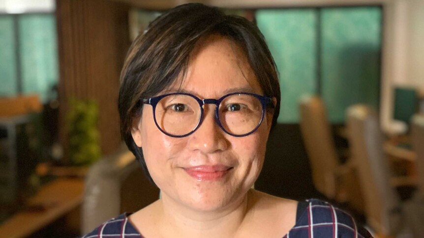 A woman with short hair and black glasses with a navy checked dress shirt.