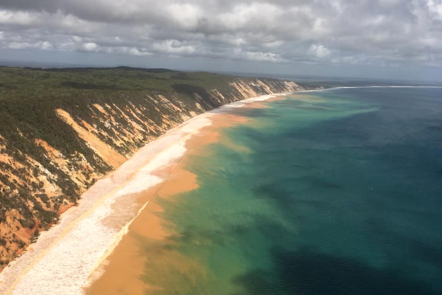 An aerial photo shows waves washing sand from Rainbow Beach into the ocean.