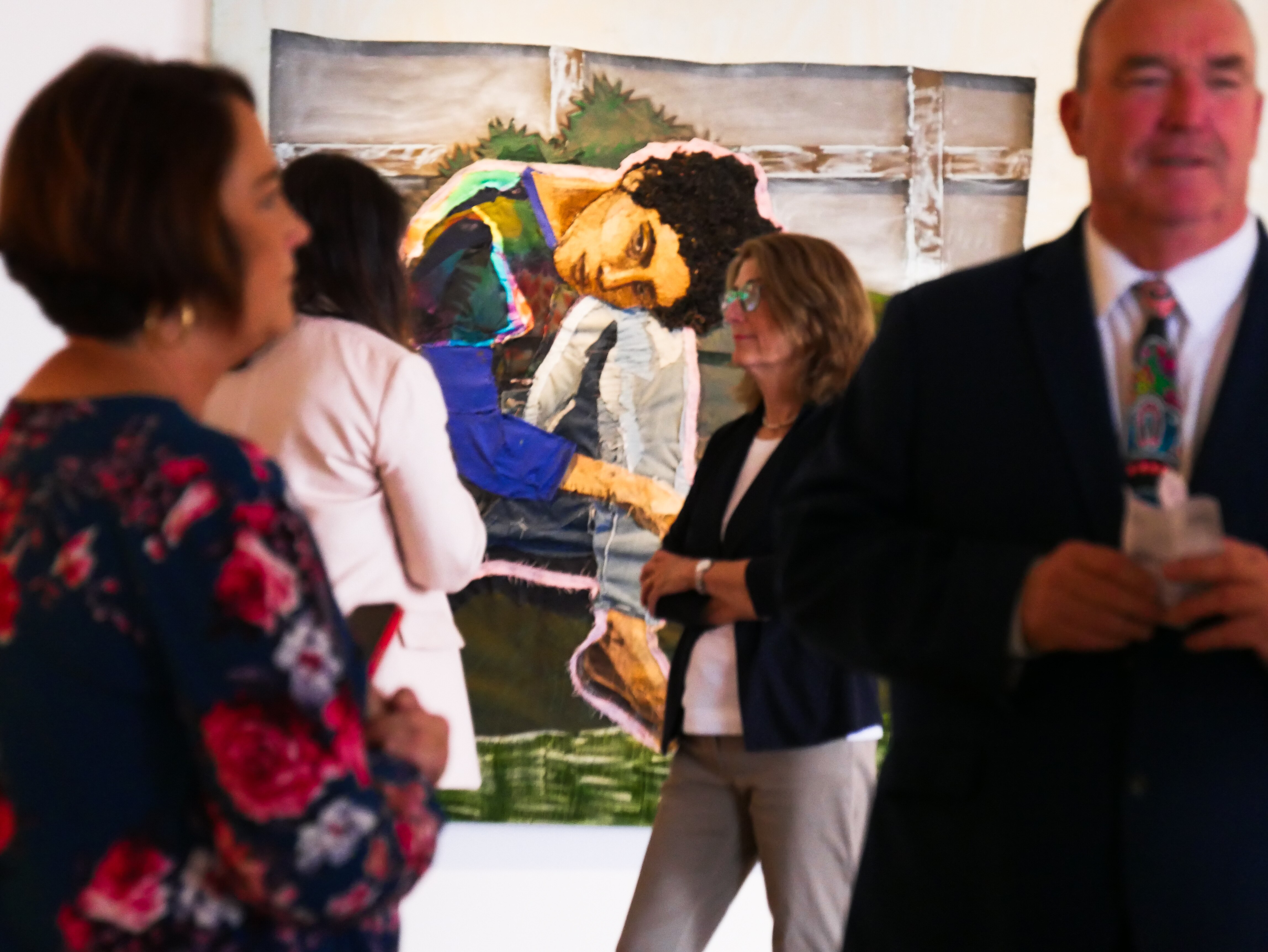a group of people stand in a gallery with a beautiful piece of art in the background