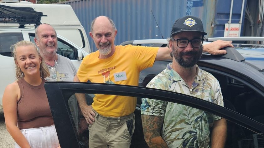 man wearing a hat standing near the drivers seat of his car surrounded by volunteers from Resilient Lismore