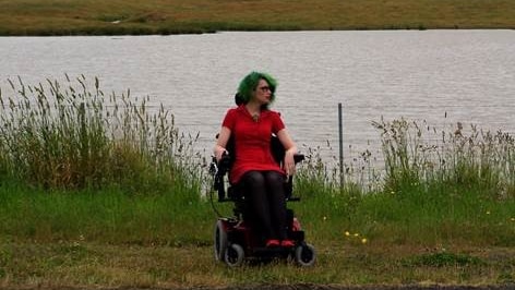 A woman in her wheelchair on the side of the road in the countryside