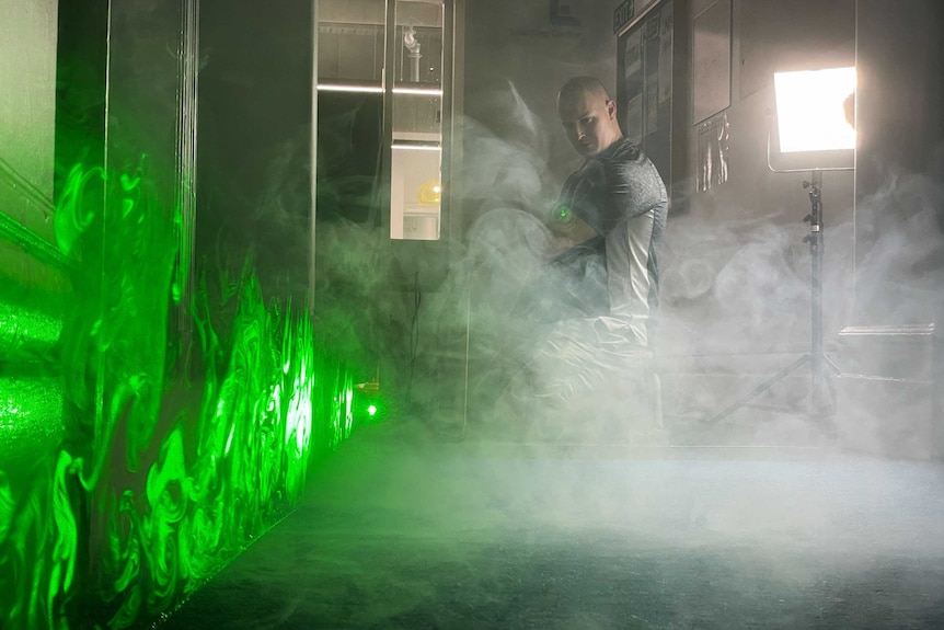 A man observes the effect of a smoke machine and how the particles are moving through the light emitted by a green laser.