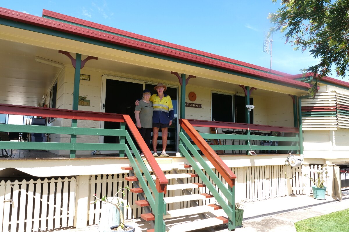 Cheryl and Trevor standing next to each other at the top of the stairs, roof over their heads and house in the background.
