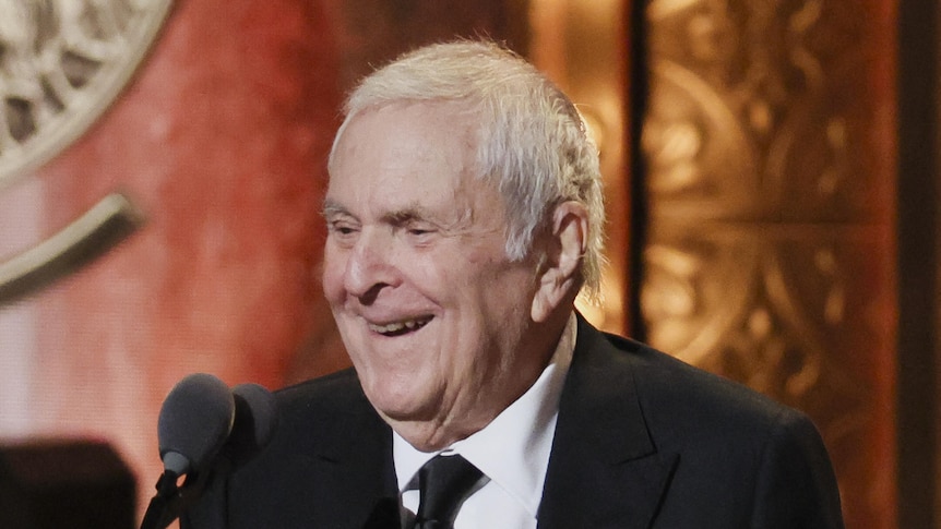 John Kander, an elderly white man in a suit, accepts an award onstage at the 2023 Tony Awards.