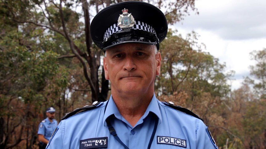 Headshot of a police officer in uniform, with bushland in the background.