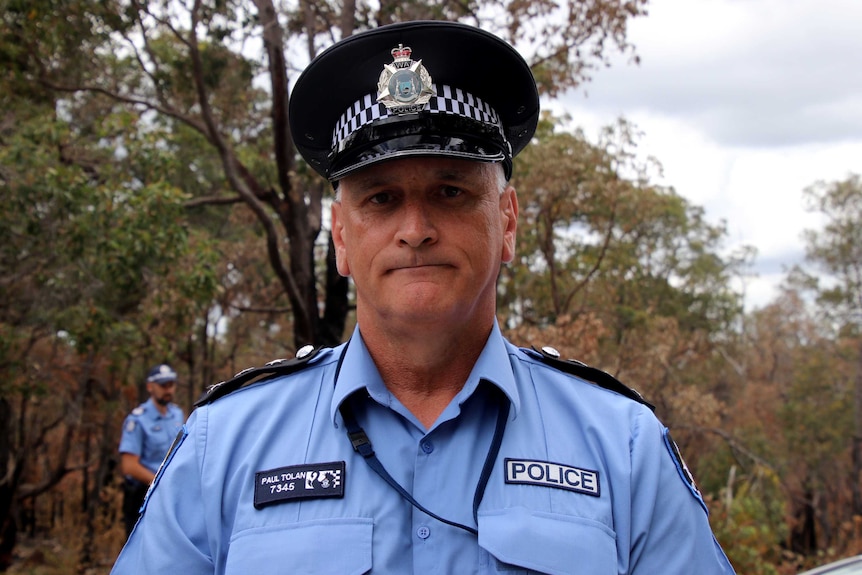 Headshot of a police officer in uniform, with bushland in the background.