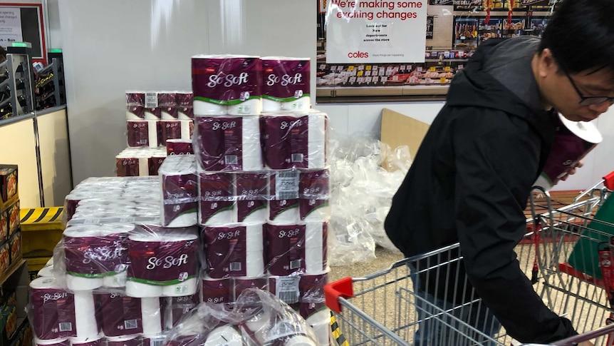 A shopper fills a trolley with toilet paper