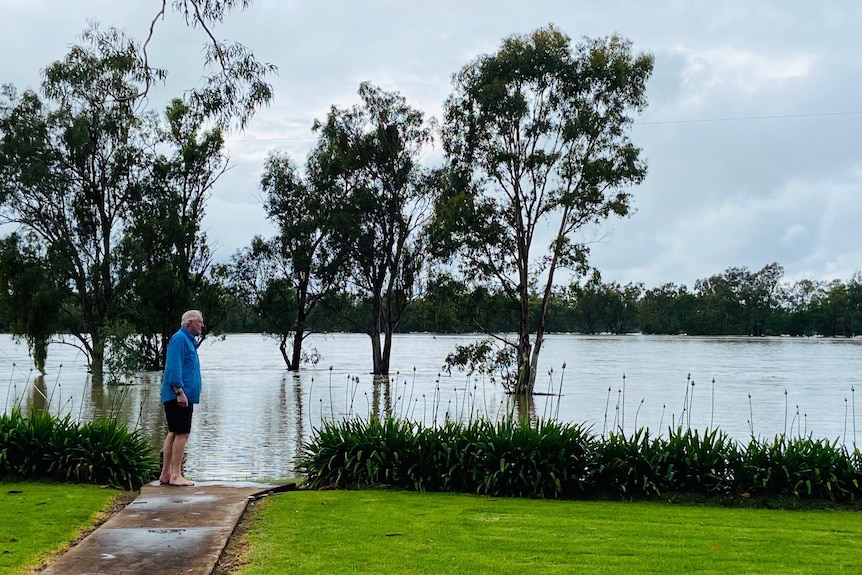 A man stands looking out at floodwaters.