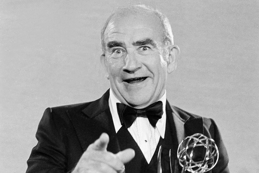A black and white photo of Ed Asner poses with his Emmy statuette