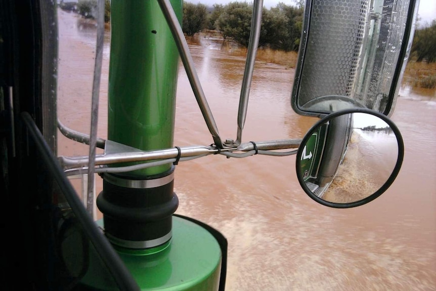 A truck's side mirror the vehicle is in the middle of brown floodwaters.