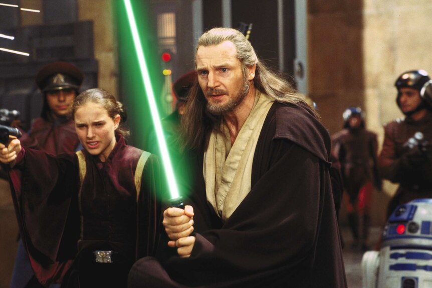 Liam Neeson, Natalie Portman in robes holding lightsabers