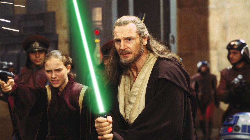 Liam Neeson, Natalie Portman in robes holding lightsabers