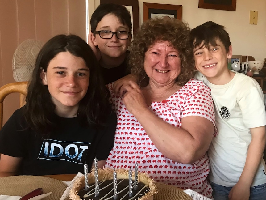 A woman with curly brown hair in a white and red spot top surrounded by three young boys with dark brown hair.