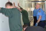 Prisoners with their hands against the walls inside Bunbury Prison, as officers search them for drugs.