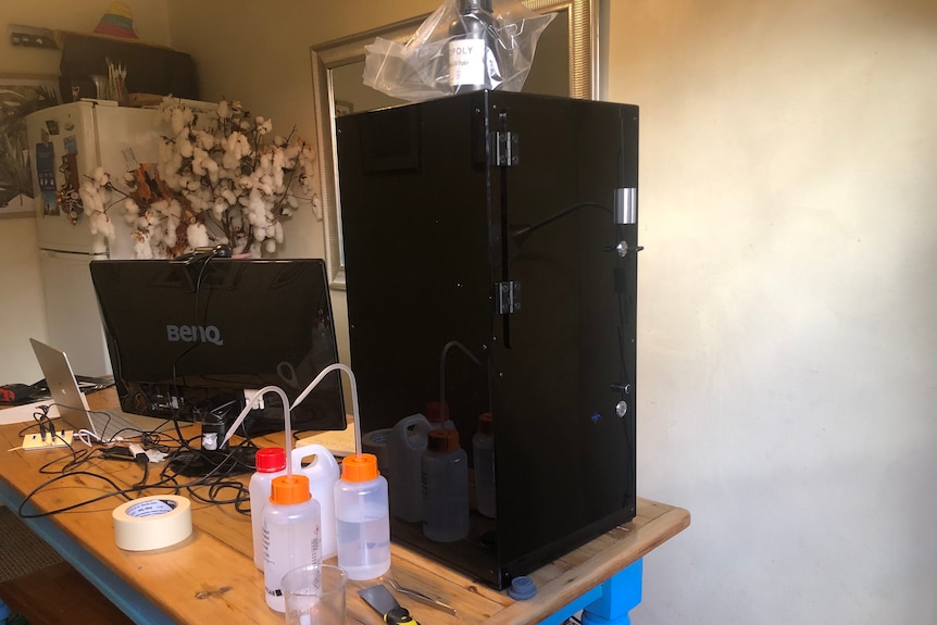 A black 3D printer sits on a dining table next to a monitor.