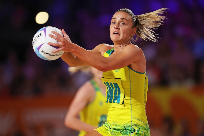 An Australian netball player holds the ball in both hands against England.