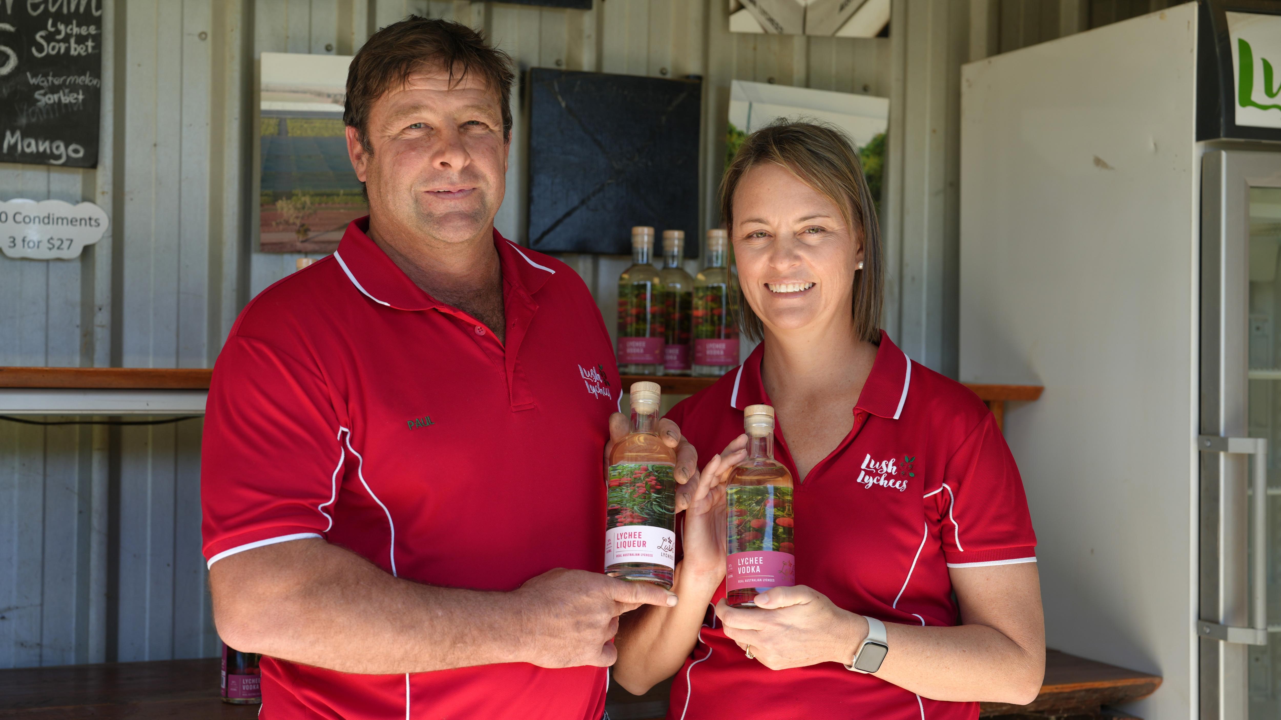 Man and woman in red uniform shirts holding bottles of clear alcohol and smiling
