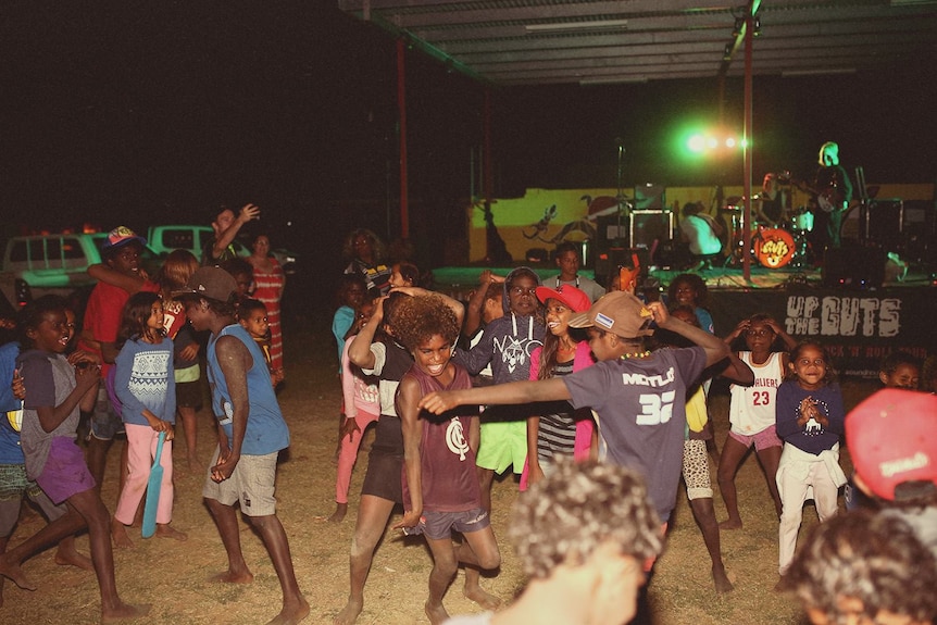 Kids dance at an outdoor gig during the evening.