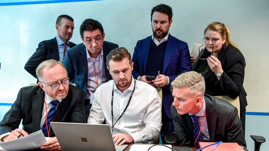 AFP officers sit with the ABC Legal team and an IT specialist all looking at a laptop.