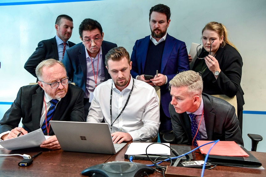 AFP officers sit with the ABC Legal team and an IT specialist all looking at a laptop.