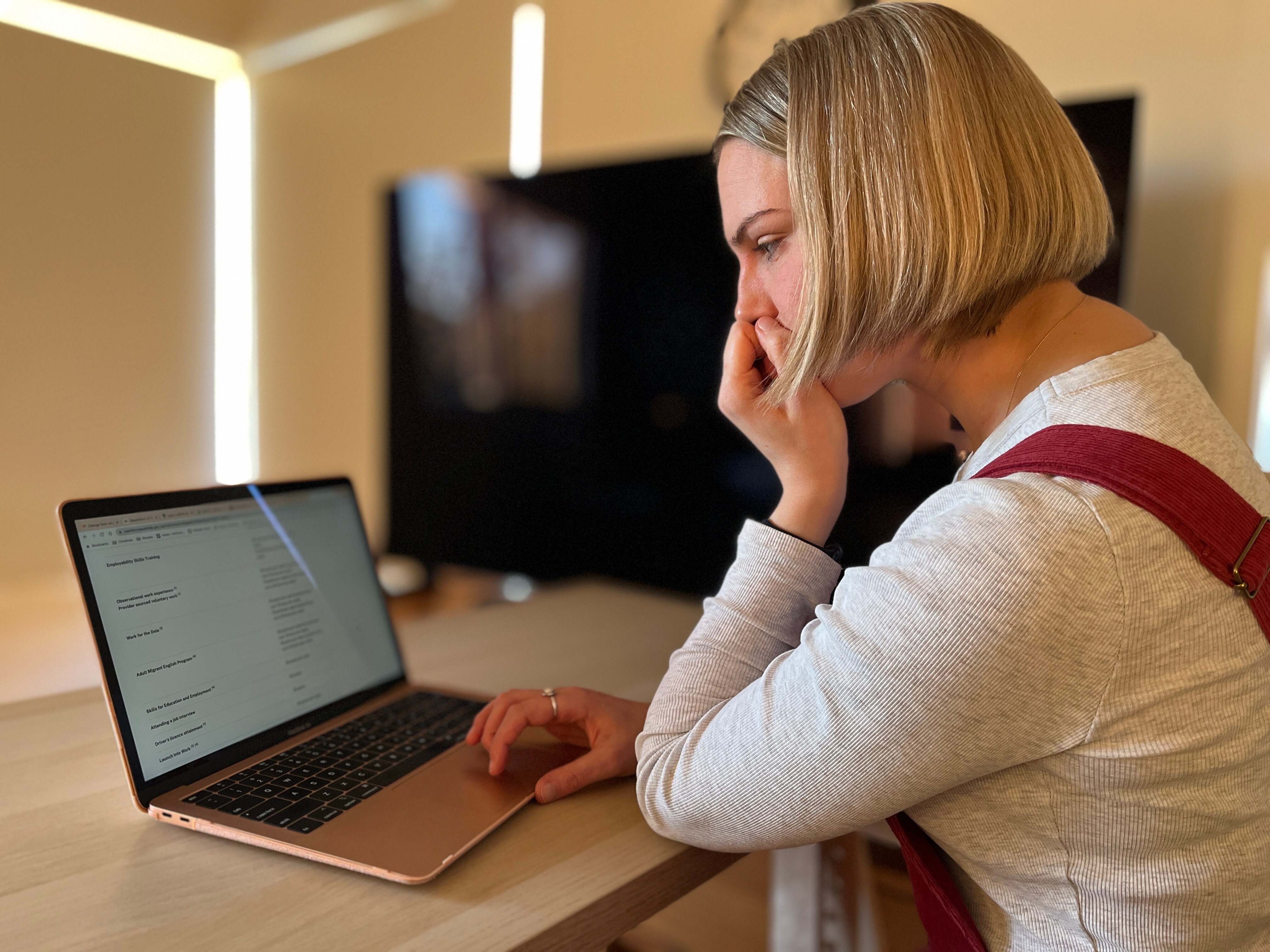A white woman with blonde hair and red overalls looking at a computer screen