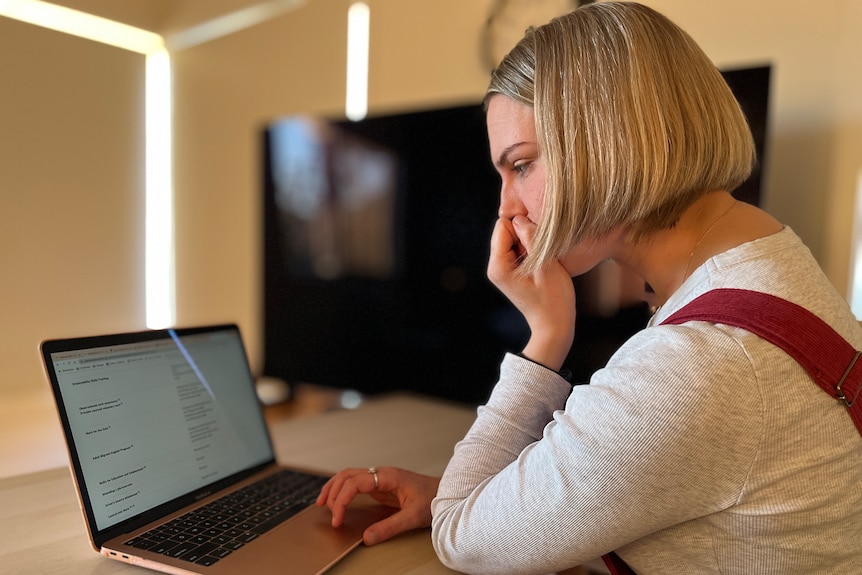 A white woman with blonde hair and red overalls looking at a computer screen