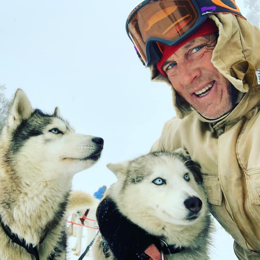 A man wearing ski gear with two Siberian huskies