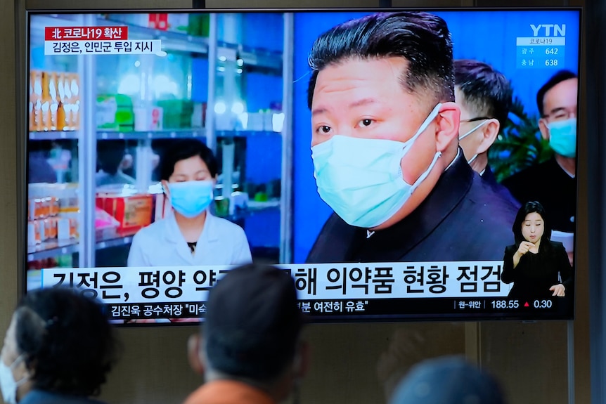 People watch television screen showing Korean news program with image of North Korean leader.