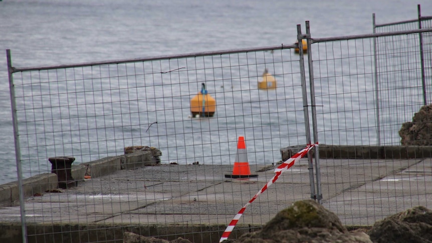 A fence and traffic cones surround a jetty with a corner piece missing.