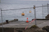 A fence and traffic cones surround a jetty with a corner piece missing.