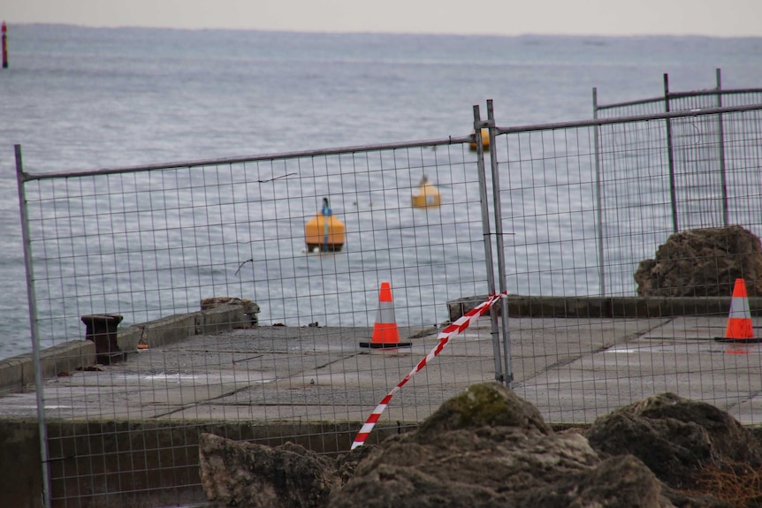 A fence and traffic cones surround a jetty with a corner piece missing.