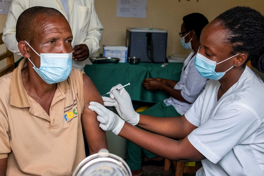 A man in a face mask receives an injection from a masked nurse