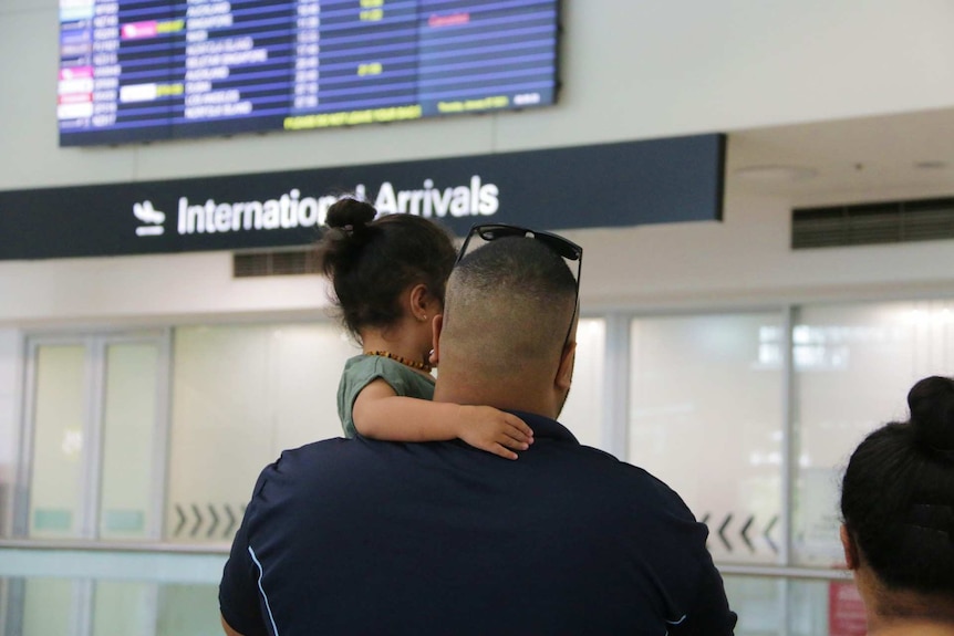 The back of a man hugging a child in an airport.